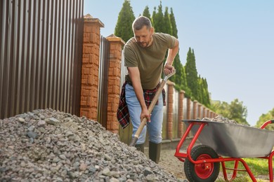 Man picking stones up with shovel and wheelbarrow outdoors