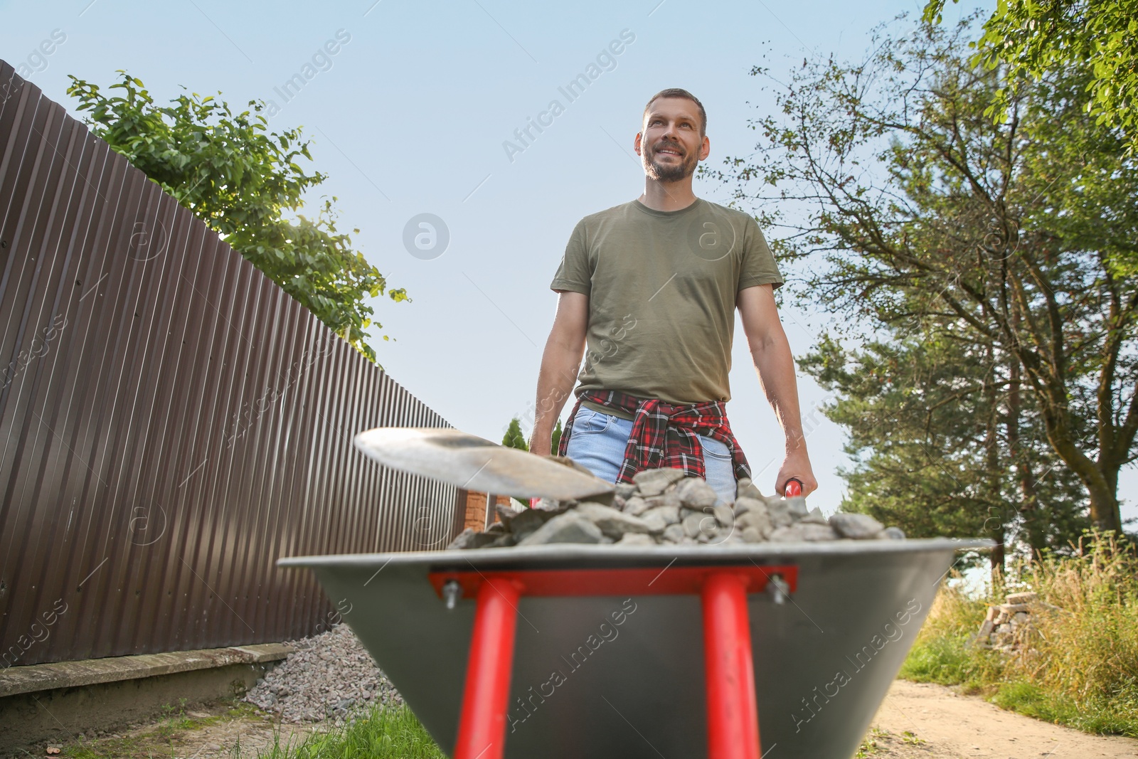 Photo of Man pushing wheelbarrow full of stones and shovel outdoors, low angle view