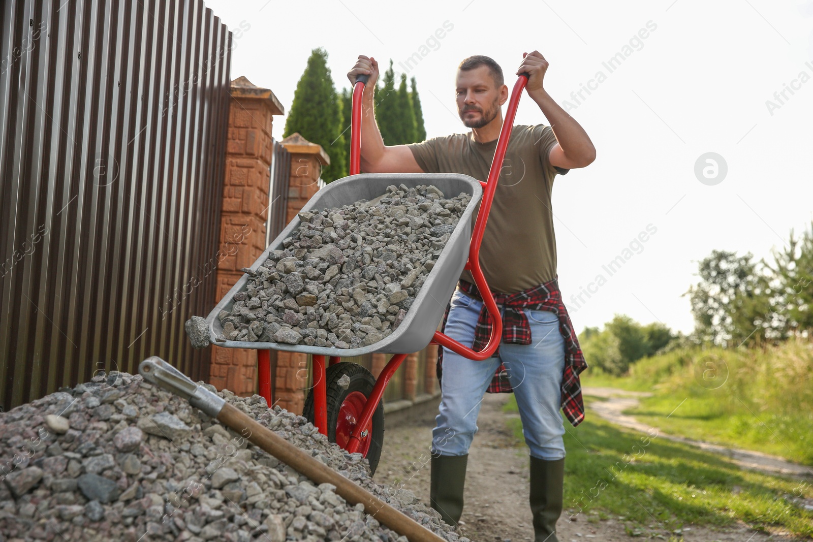 Photo of Man pouring stones out of wheelbarrow outdoors