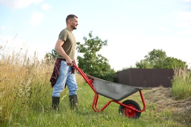 Photo of Farmer in rubber boots pushing wheelbarrow outdoors