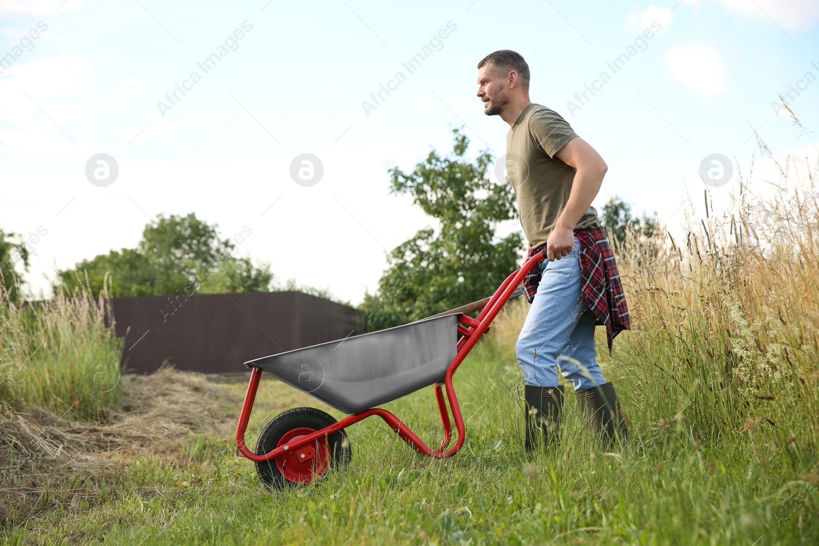 Photo of Farmer in rubber boots pushing wheelbarrow outdoors