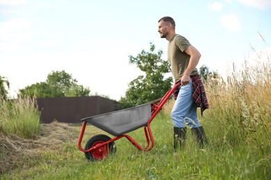 Photo of Farmer in rubber boots pushing wheelbarrow outdoors