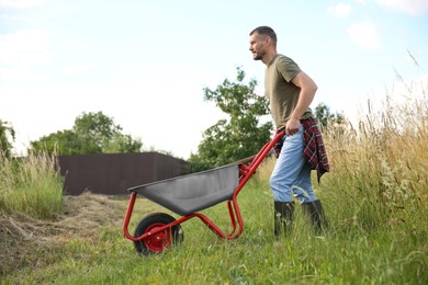 Farmer in rubber boots pushing wheelbarrow outdoors