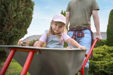 Father pushing wheelbarrow with his daughter outdoors, closeup