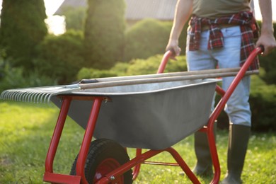 Man with wheelbarrow and gardening tools outdoors on sunny day, closeup