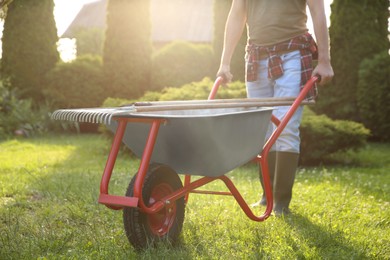 Photo of Man with wheelbarrow and gardening tools outdoors on sunny day, closeup