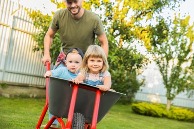 Photo of Father pushing wheelbarrow with his kid outdoors, space for text