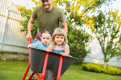 Father pushing wheelbarrow with his kid outdoors, space for text