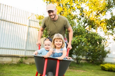 Photo of Father pushing wheelbarrow with his kid outdoors
