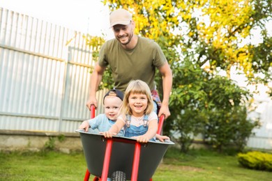 Father pushing wheelbarrow with his kid outdoors