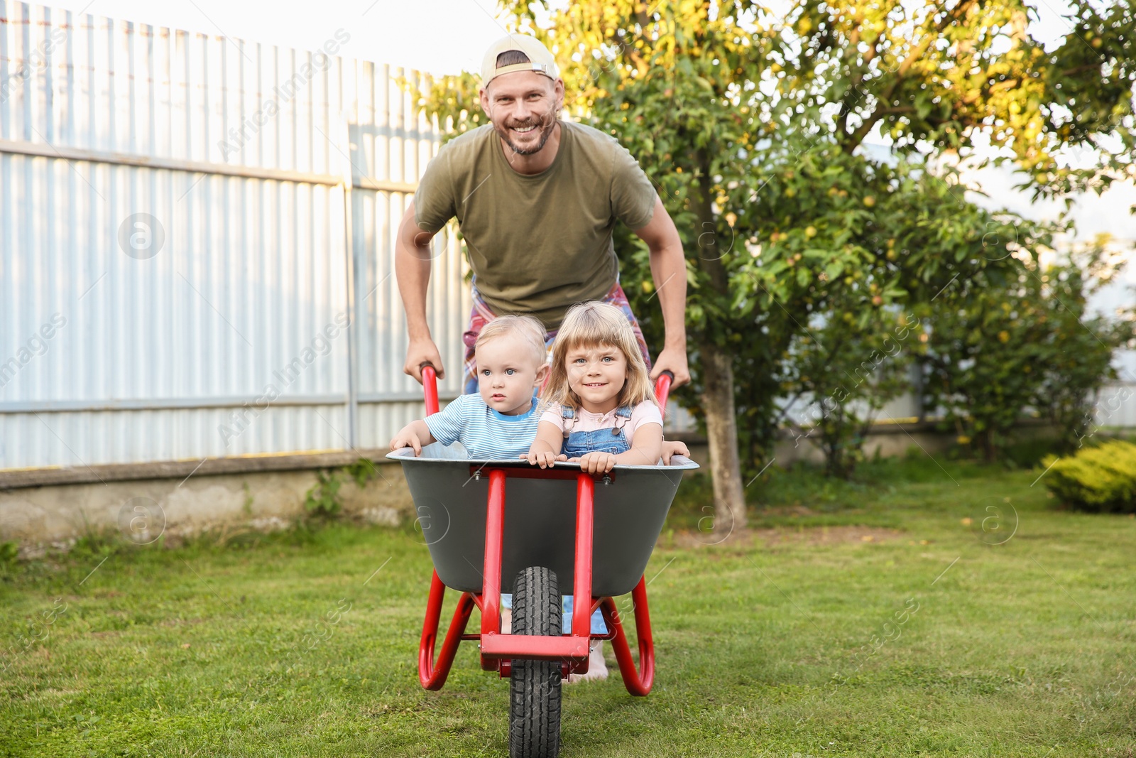 Photo of Father pushing wheelbarrow with his kid outdoors