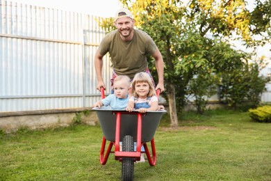 Father pushing wheelbarrow with his kid outdoors