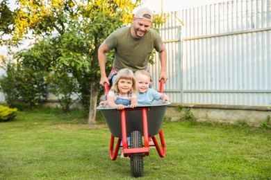 Photo of Father pushing wheelbarrow with his kid outdoors