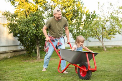 Father pushing wheelbarrow with his daughter outdoors