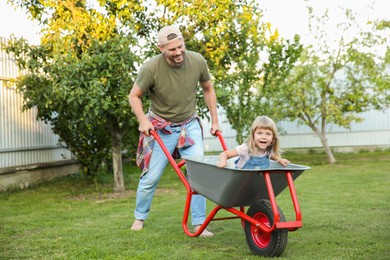 Father pushing wheelbarrow with his daughter outdoors