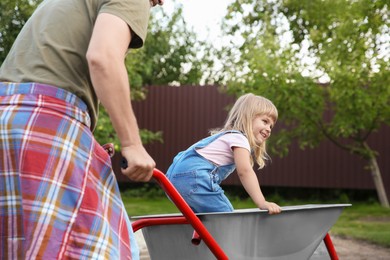 Photo of Father pushing wheelbarrow with his daughter outdoors, closeup