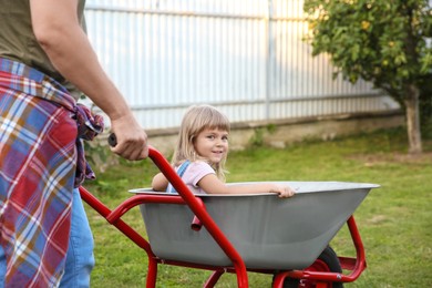 Father pushing wheelbarrow with his daughter outdoors, closeup