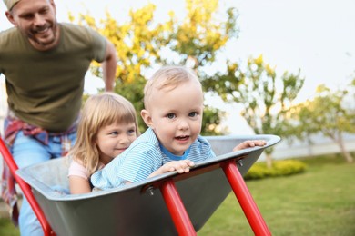 Photo of Father pushing wheelbarrow with his kids outdoors