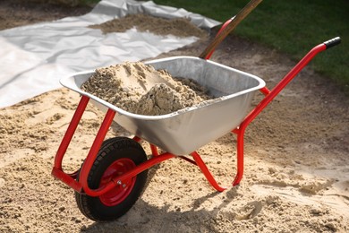 Metal wheelbarrow with pile of sand outdoors