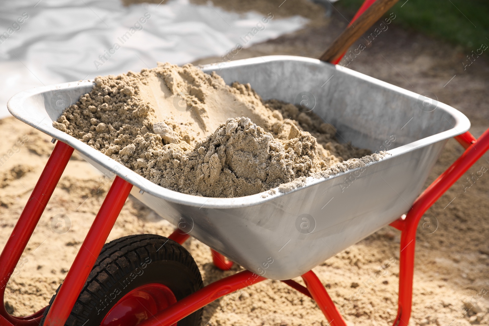 Photo of Metal wheelbarrow with pile of sand outdoors, closeup