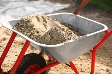 Metal wheelbarrow with pile of sand outdoors, closeup