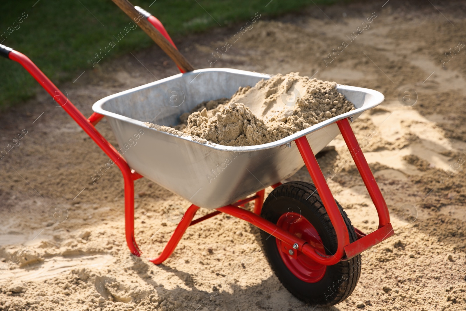 Photo of Metal wheelbarrow with pile of sand outdoors