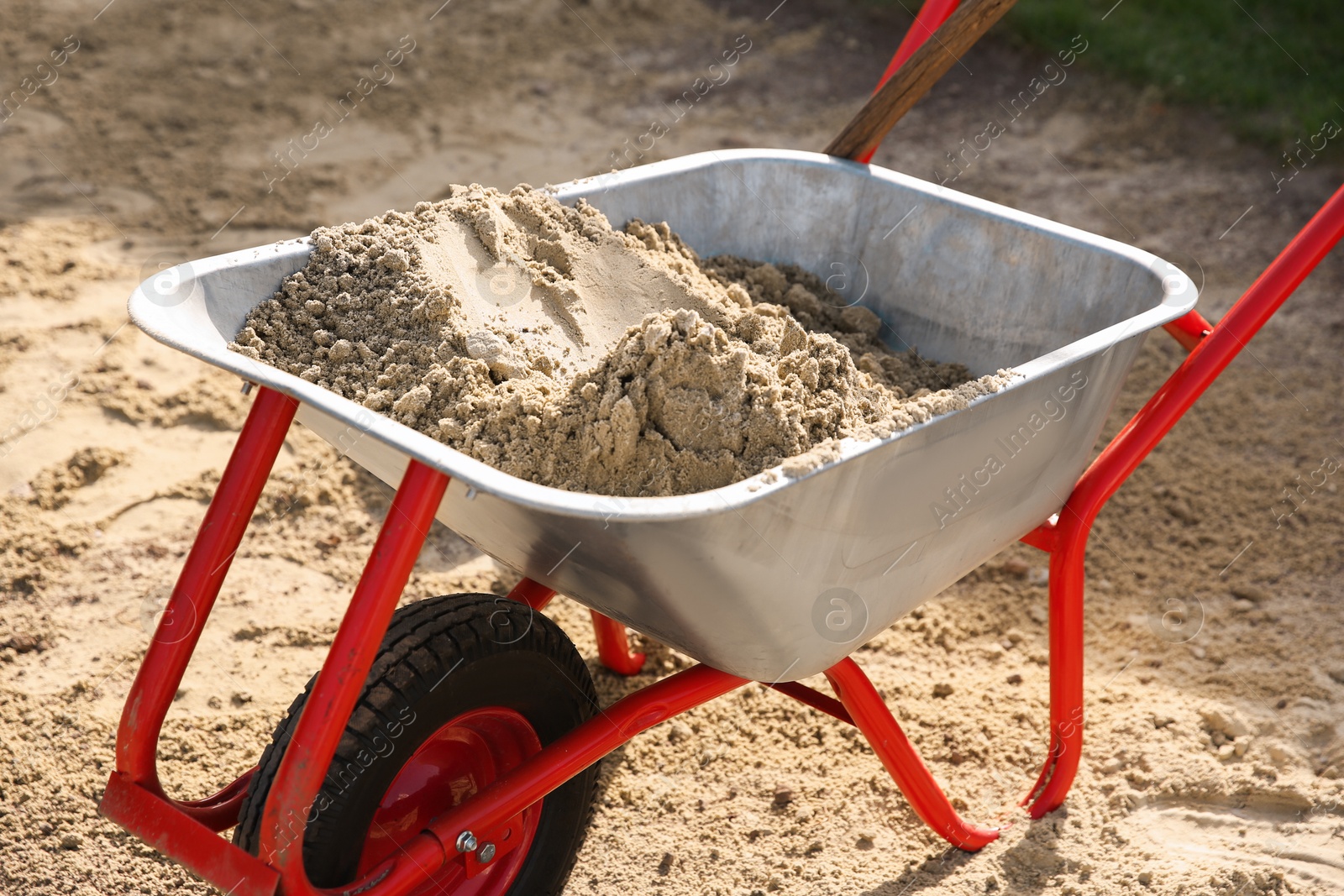 Photo of Metal wheelbarrow with pile of sand outdoors