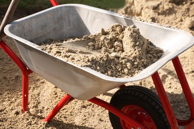 Metal wheelbarrow with pile of sand outdoors, closeup