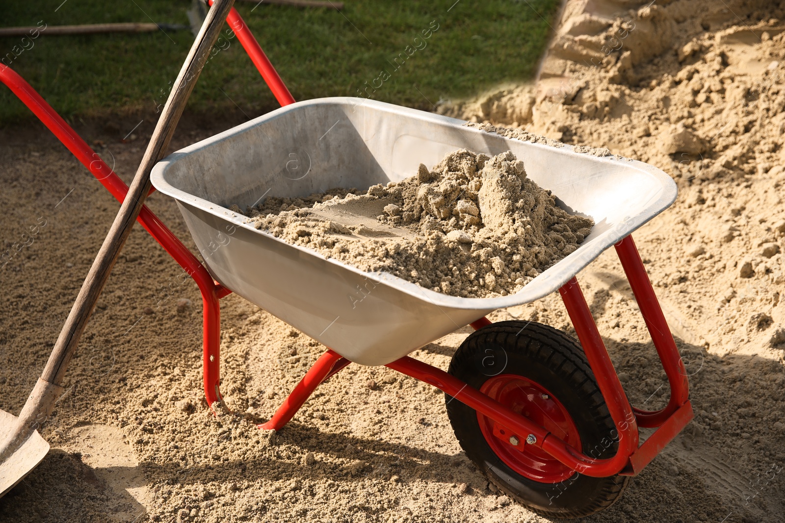 Photo of Metal wheelbarrow with pile of sand and shovel outdoors