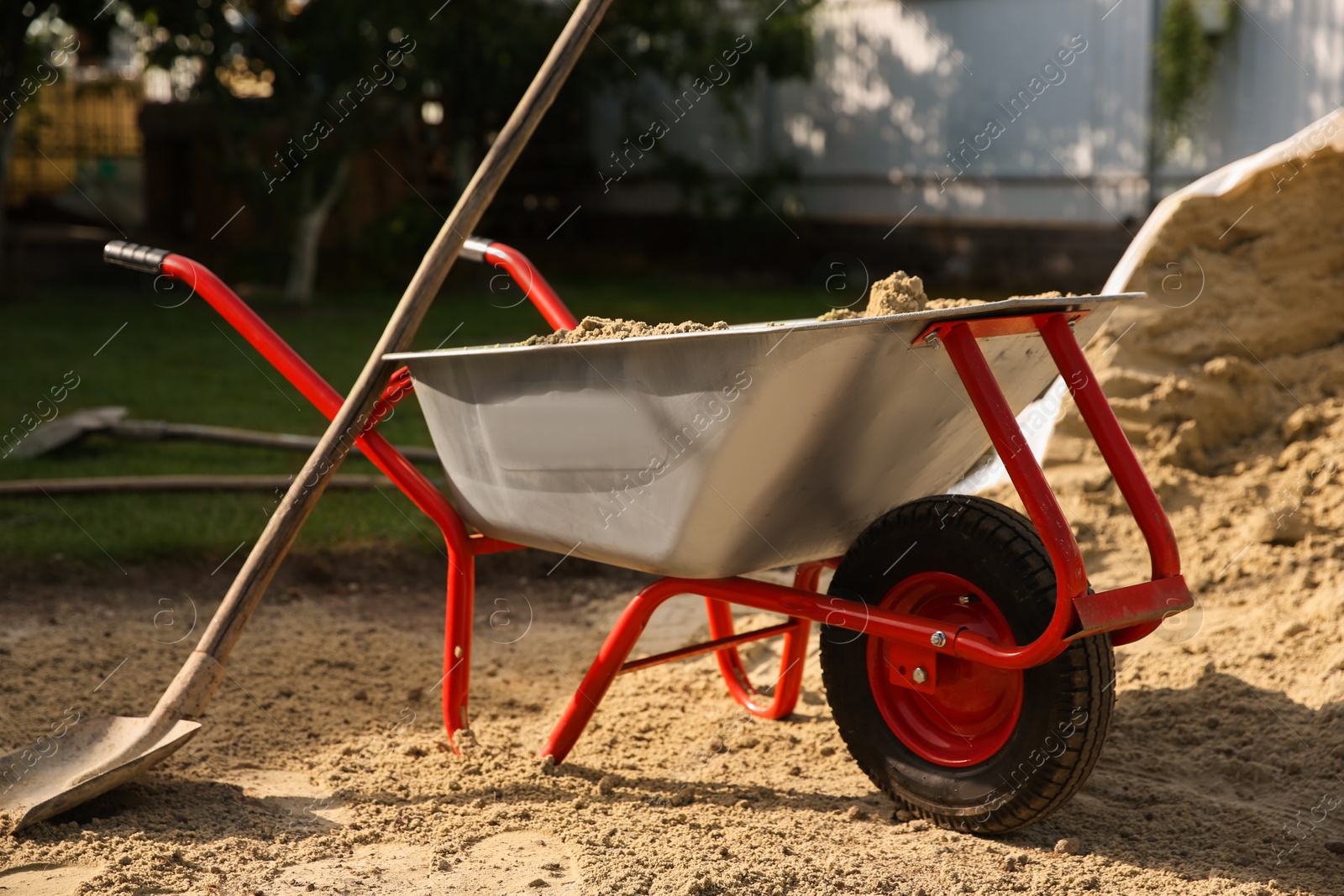 Photo of Metal wheelbarrow and shovel on sand outdoors