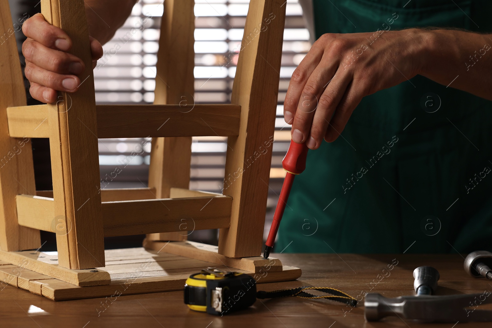 Photo of Man repairing wooden stool with screwdriver indoors, closeup