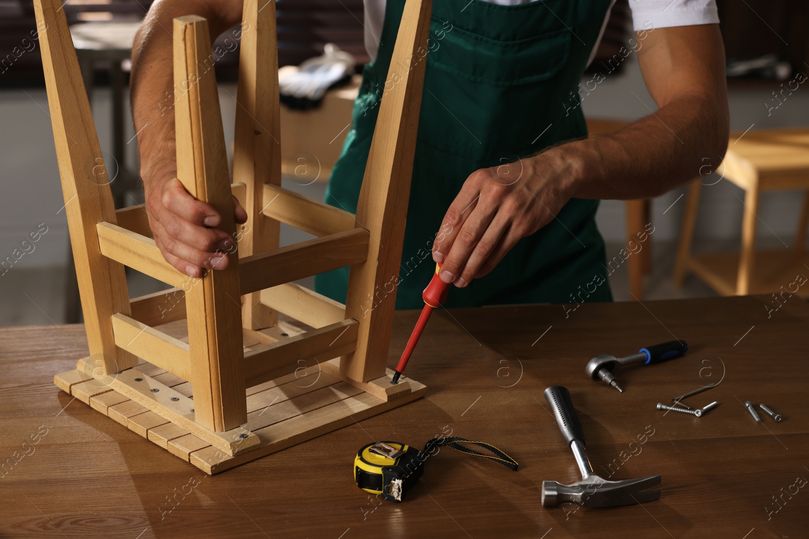 Photo of Man repairing wooden stool with screwdriver indoors, closeup