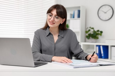 Photo of Smiling secretary doing paperwork at table in office