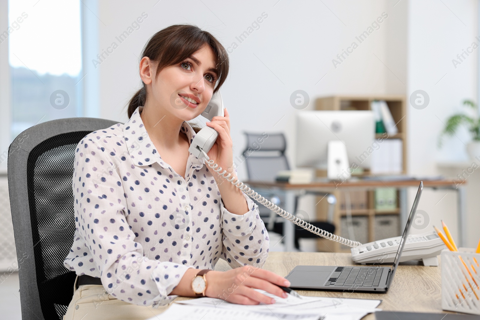 Photo of Smiling secretary talking on telephone at table in office