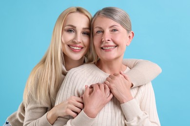 Family portrait of young woman and her mother on light blue background