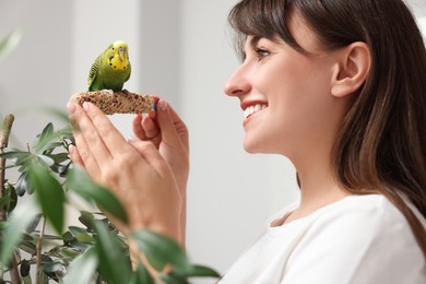 Woman feeding bright parrot with bird treat indoors. Exotic pet