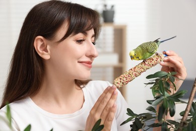 Woman feeding bright parrot with bird treat indoors. Exotic pet