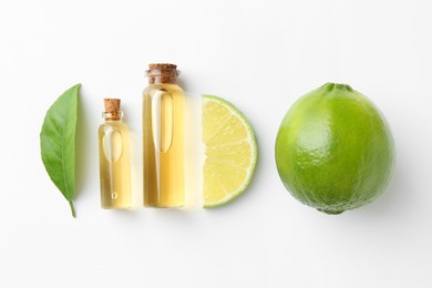 Bottles of essential oils, lime and green leaf on white background, flat lay