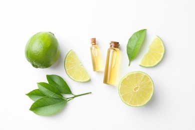 Photo of Bottles of essential oils, lime and green leaves on white background, flat lay