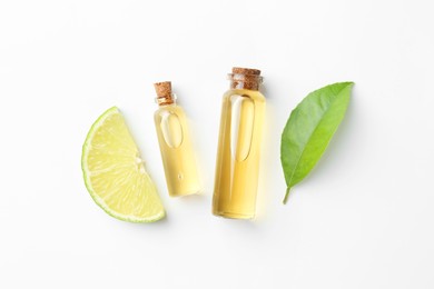 Photo of Bottles of essential oils, lime and green leaf on white background, flat lay