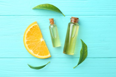 Photo of Bottles of essential oils, orange and green leaves on turquoise wooden table, flat lay