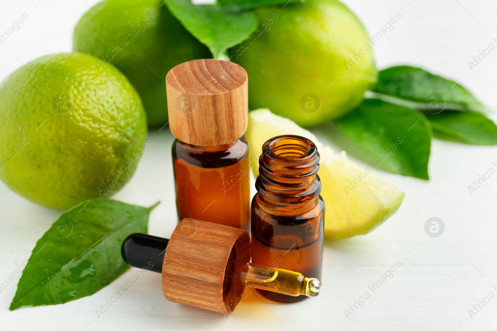 Photo of Essential oils in bottles, dropper, limes and green leaves on white table, closeup