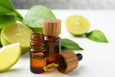 Photo of Essential oils in bottles, dropper, limes and green leaves on white table, closeup