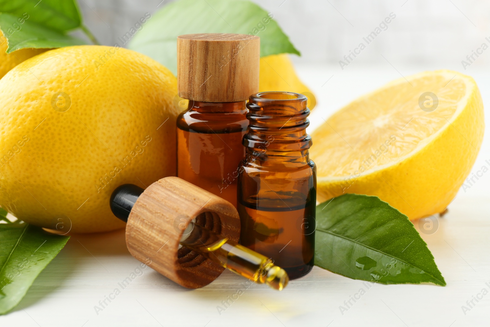 Photo of Essential oils in bottles, dropper, lemons and green leaves on white table, closeup