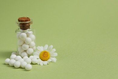 Photo of Bottle of homeopathic remedy and chamomile on light green background. Space for text