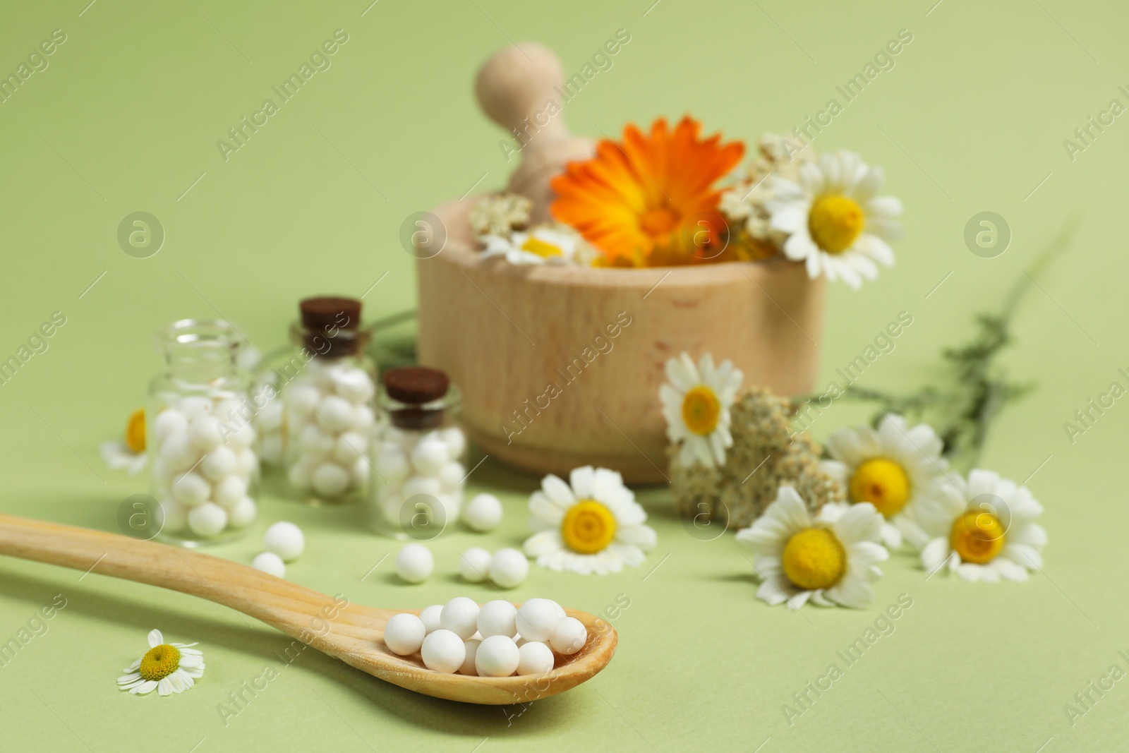 Photo of Homeopathic remedy, mortar and flowers on light green background, selective focus