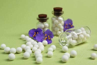 Bottles with homeopathic remedy and flowers on light green background, closeup