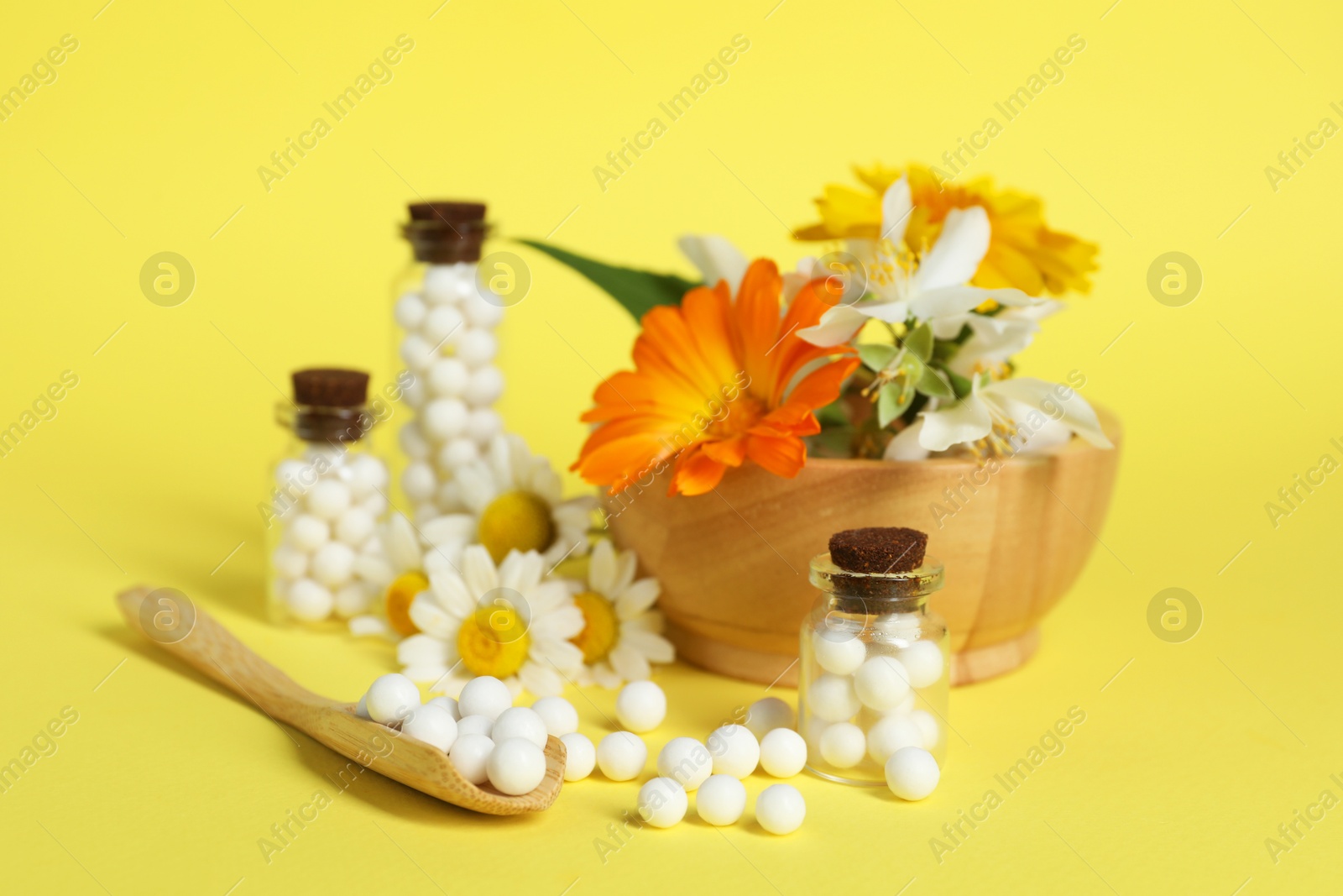 Photo of Homeopathic remedy and flowers on yellow background, closeup