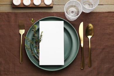 Photo of Empty menu, plates, cutlery, glasses and decor on wooden table, top view. Mockup for design