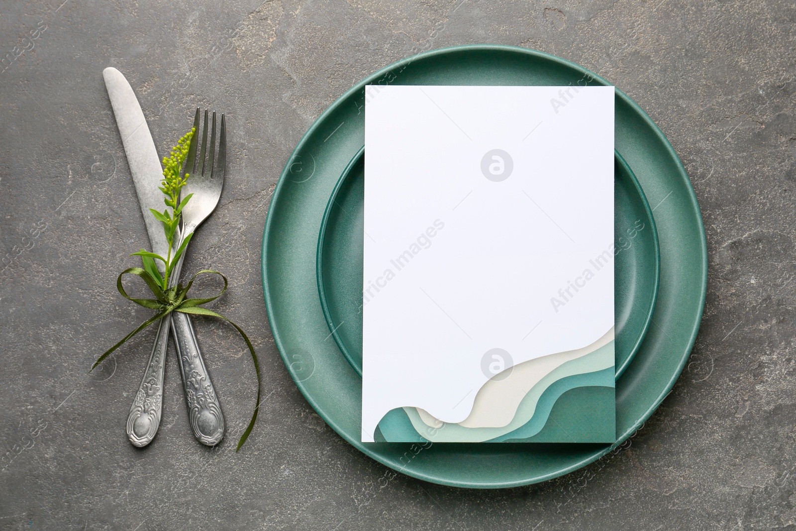 Photo of Empty menu, plates, cutlery and floral decor on grey table, top view. Mockup for design